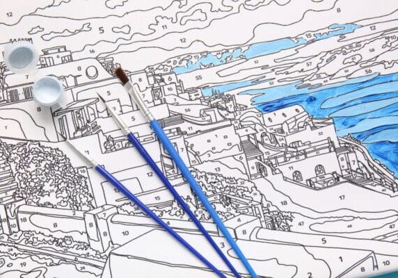 Pintura por números com três pincéis e parte do mar pintada de azul.